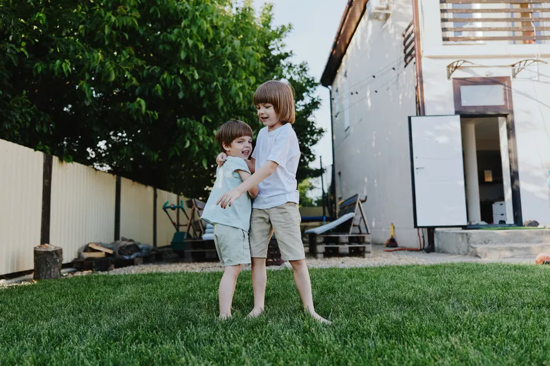 Playful boys hugging in a sunny garden, enjoying childhood moments surrounded by greenery and a cheerful atmosphere in the backyard.