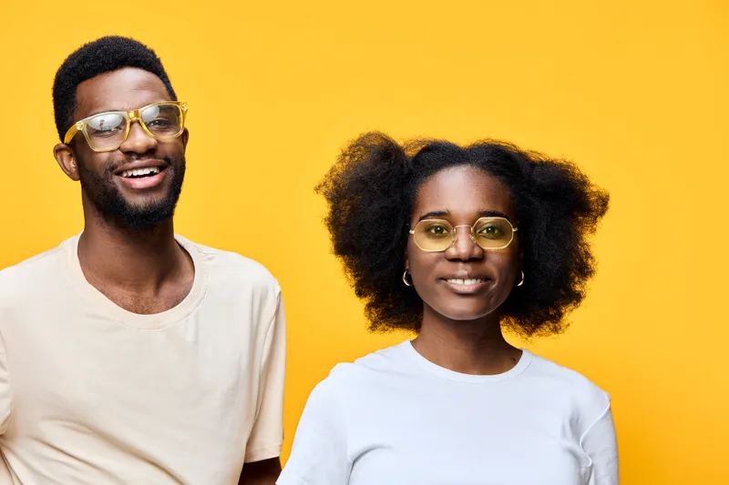A joyful African couple wearing stylish glasses against a bright yellow background, expressing happiness and confidence in casual attire