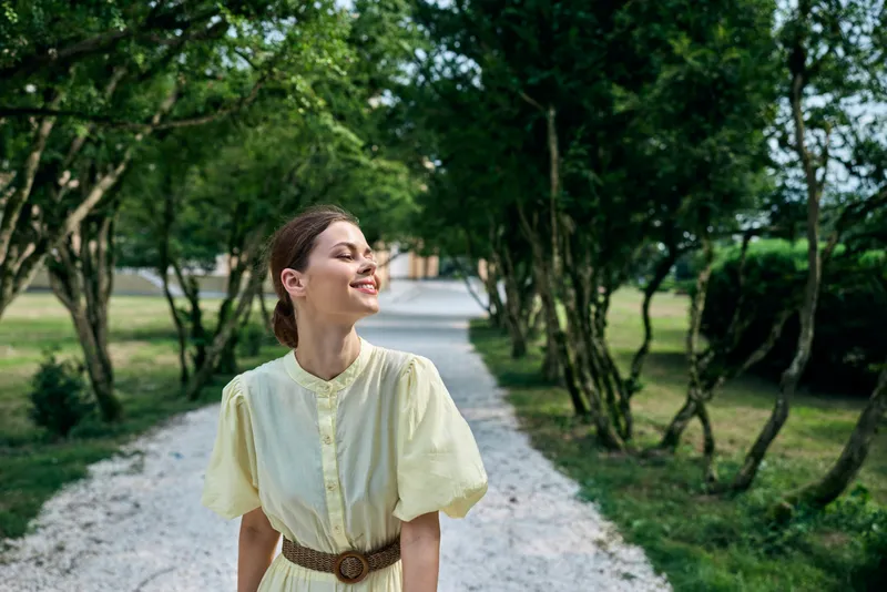 Woman smile outdoors on park pathway in dress, trees and gravel road, portrait with authenticity inclusivity and calm tone