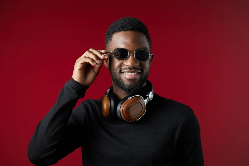 Smiling young man in sunglasses wearing headphones, showcasing confidence against a vibrant red background, ideal for music or lifestyle themes
