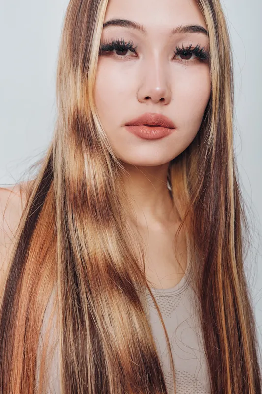 Young woman with long blonde hair and natural makeup poses in studio with neutral background wearing casual tank top showing beauty and fashion style.