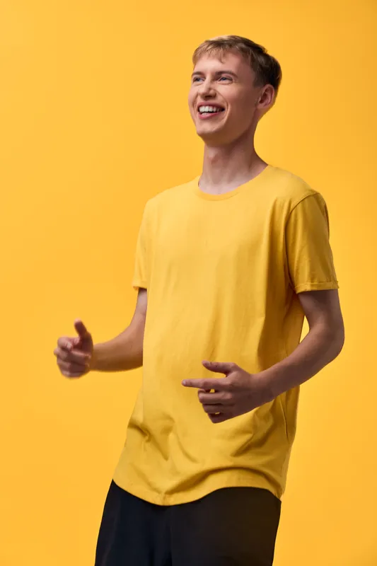 Smiling man in a yellow shirt stands in a bright studio, casual style, joyful energy and positive mood suitable for lifestyle, fashion and advertising campaigns
