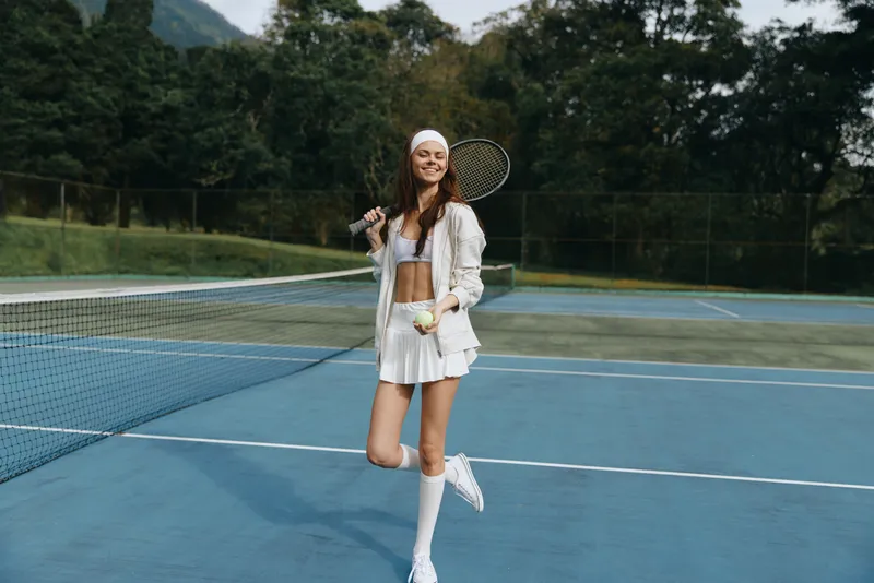Sporty young woman playing tennis outdoors in a white outfit, showcasing confidence and joy on a clear day with a blue court background