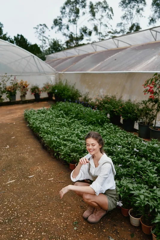 Smiling young woman gardening in lush green greenhouse, showcasing a connection with nature and healthy lifestyle while promoting organic farming and sustainability