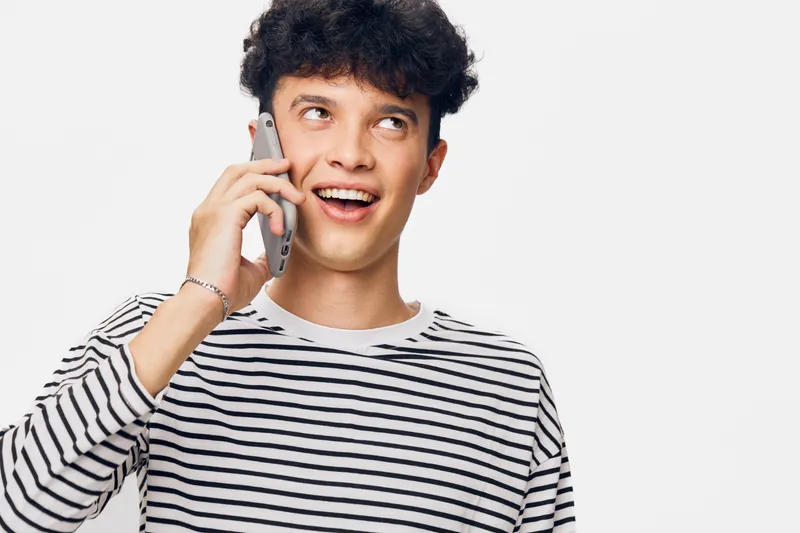 young man talking on smartphone with happy expression, striped shirt, curly hair, isolated white background, positive communication concept photo.