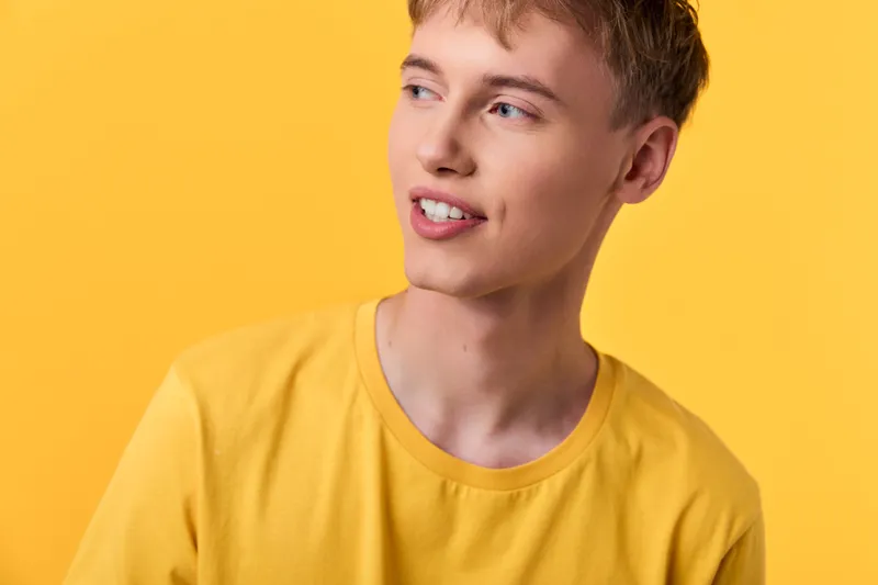 Man with a bright smile wearing a yellow shirt against a vibrant yellow backdrop, studio style for cheerful fashion, lifestyle or summer concept