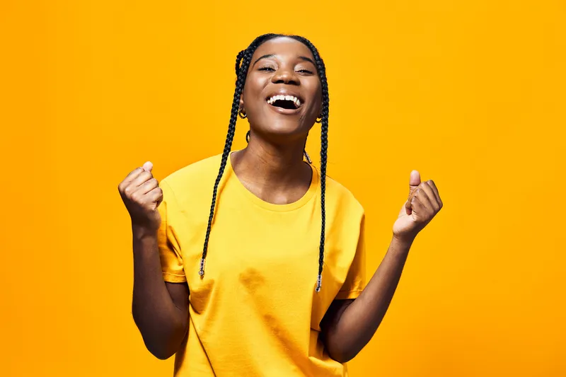 Joyful young woman celebrating success in a bright yellow t shirt against a vibrant yellow background, showcasing positivity and happiness