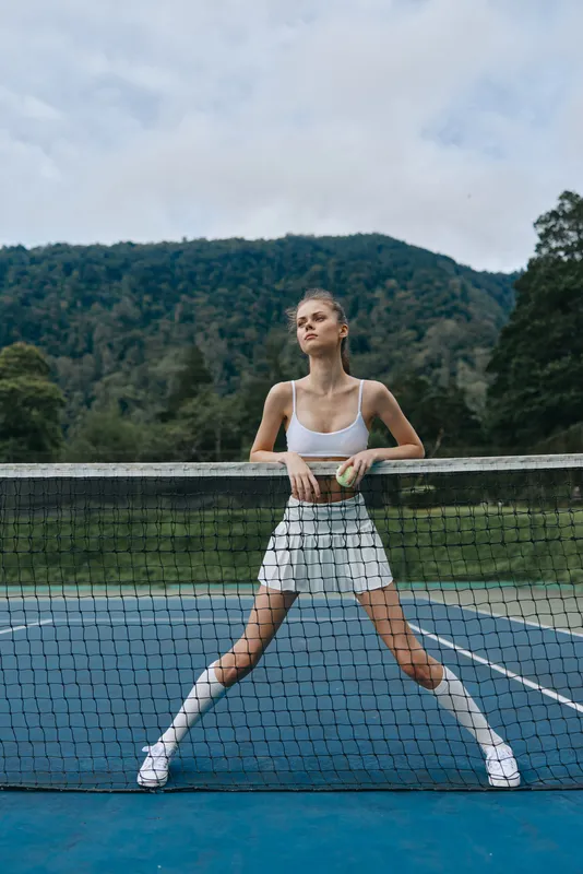 Young athletic model in tennis outfit striking a confident pose on a court, embodying sportsmanship and dedication with a vibrant outdoor backdrop