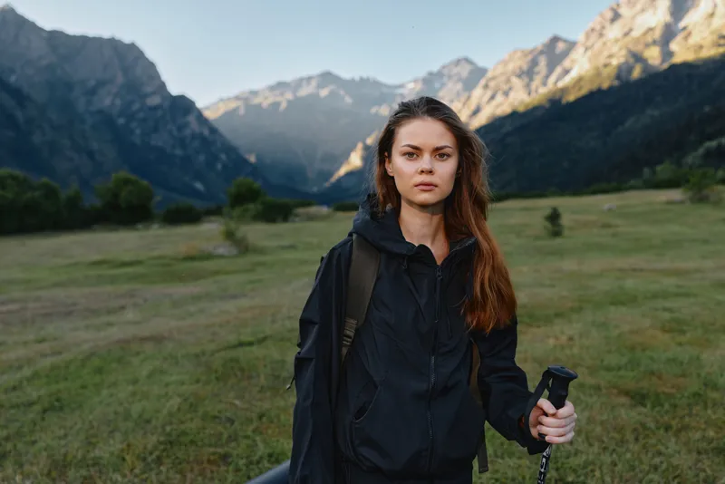 A focused trekker stands in a wide mountain valley, gear ready, gaze ahead with determination, conveying adventure, resilience, and independence in a rugged outdoor setting.