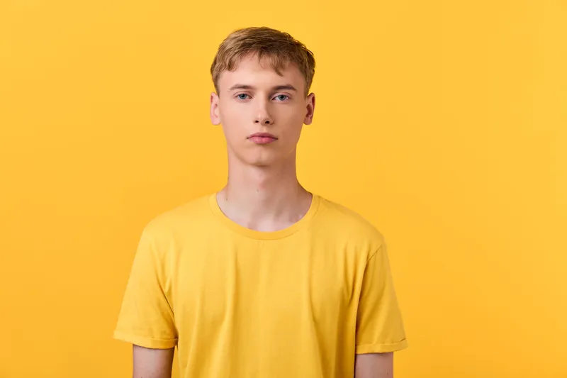 Young man wearing a bright yellow tshirt stands against a solid yellow backdrop, casual fashion vibe, clean composition with soft lighting and minimal studio styling