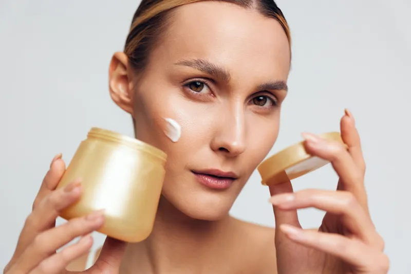 Healthy woman applying cream from a jar, closeup skincare moment, soft lighting, natural glow, relaxed expression, daily routine idea in studio, warm tones, candid pose, fresh complexion