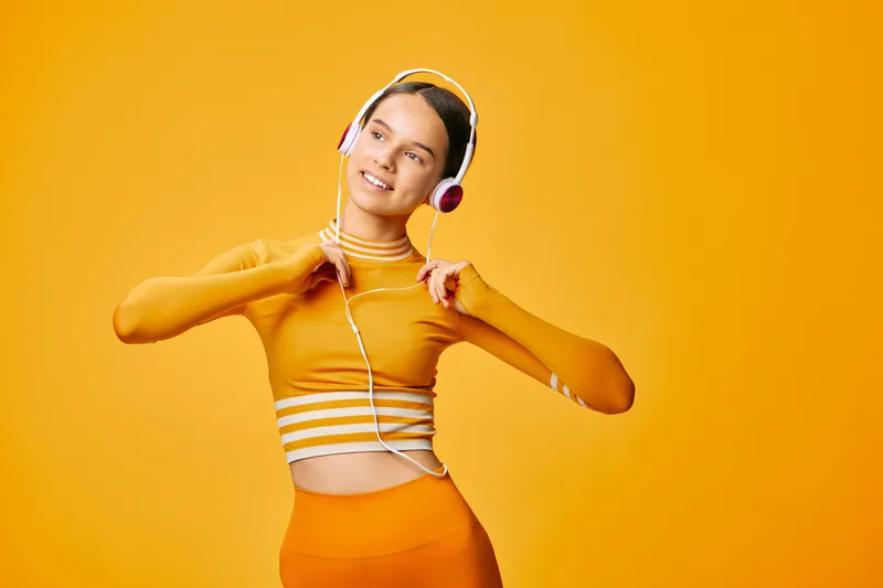 Woman in bright orange athletic wear dancing with headphones, showcasing dynamic fitness movement, energy and rhythm in a vibrant studio setting.