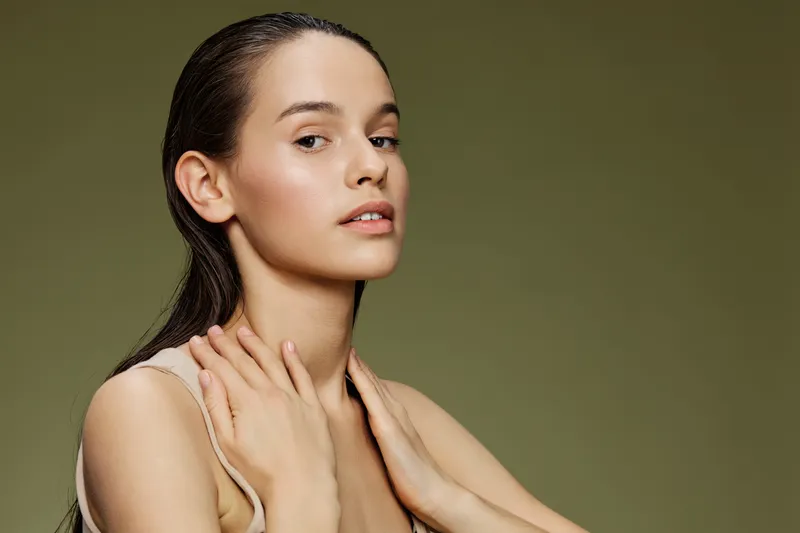 A serene portrait of a young woman with long hair against a soft green background, highlighting natural beauty, minimalist style, and a sense of calmness