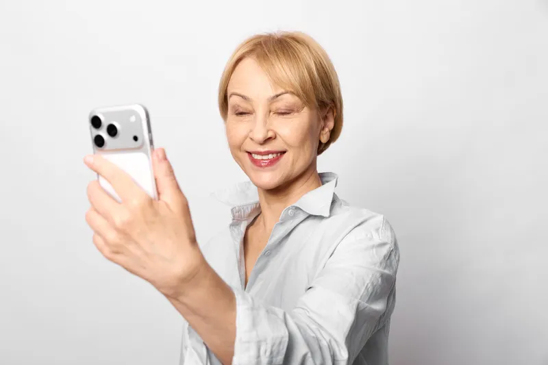 woman smartphone technology communication elderly smiling portrait white background indoor scene she holds mobile device and looks at screen for digital message or connection