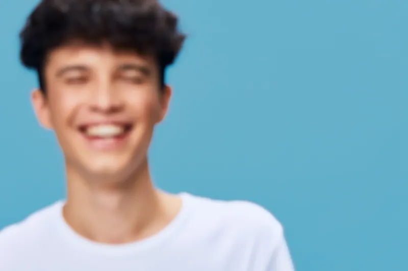 smiling man wearing white t-shirt with curly hair on blue background, expressing happiness and joy with casual style and natural lighting