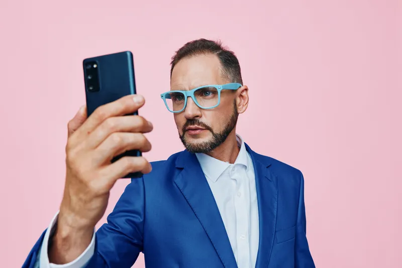 A professional man in a blue suit takes a selfie against a vibrant pink background, showcasing confidence, focus, and emotion in a modern business portrait.