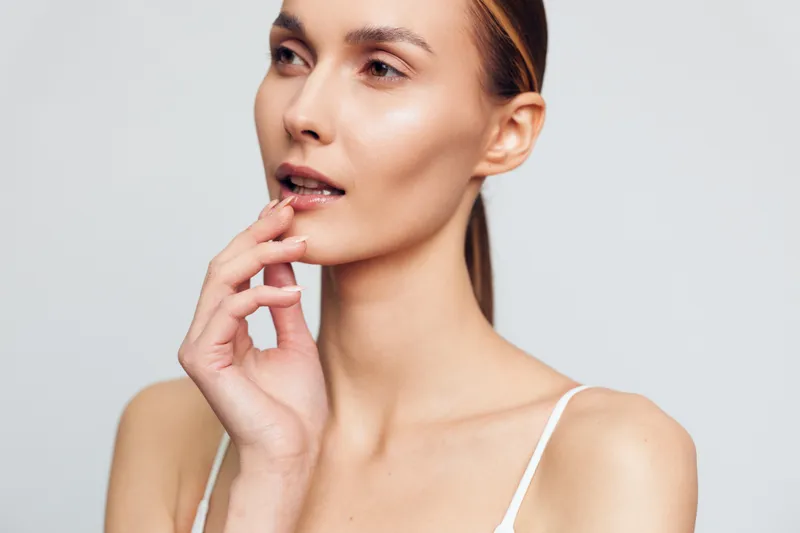 A thoughtful portrait of a woman with lips lightly touched by a finger, highlighting skincare, natural beauty, and a calm, confident expression. Focus on skin health and self care.