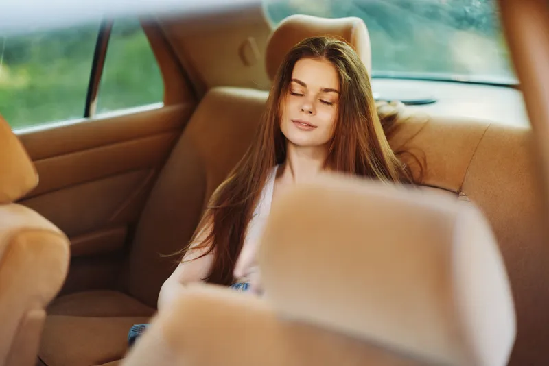 Relaxed girl resting in the back seat of a car, enjoying a peaceful moment during a sunny day trip with soft colors and a serene atmosphere.