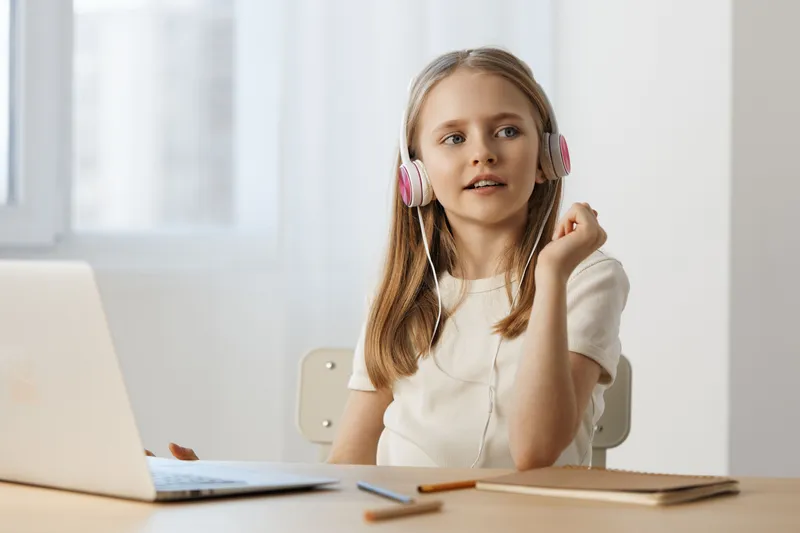 Young girl with headphones enjoying music while studying at home in a bright, airy room, reflecting happiness and concentration during online lessons