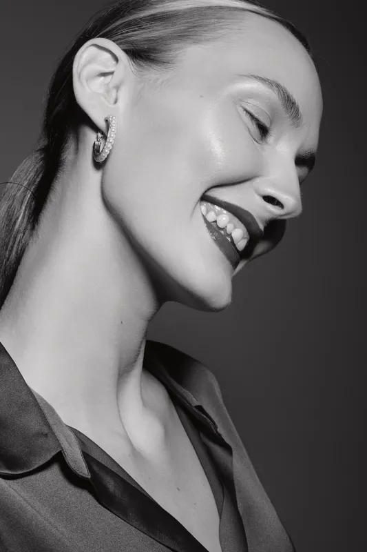 Smiling Caucasian woman with light skin and earrings in black shirt poses with closed eyes. Studio portrait with soft lighting.