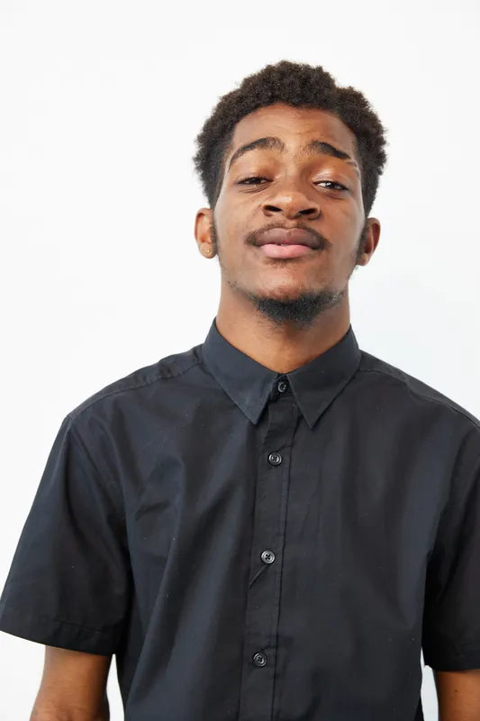 Confident African American man smiling, wearing a black shirt, showcasing a vibrant personality against a clean white backdrop, perfect for lifestyle concepts.