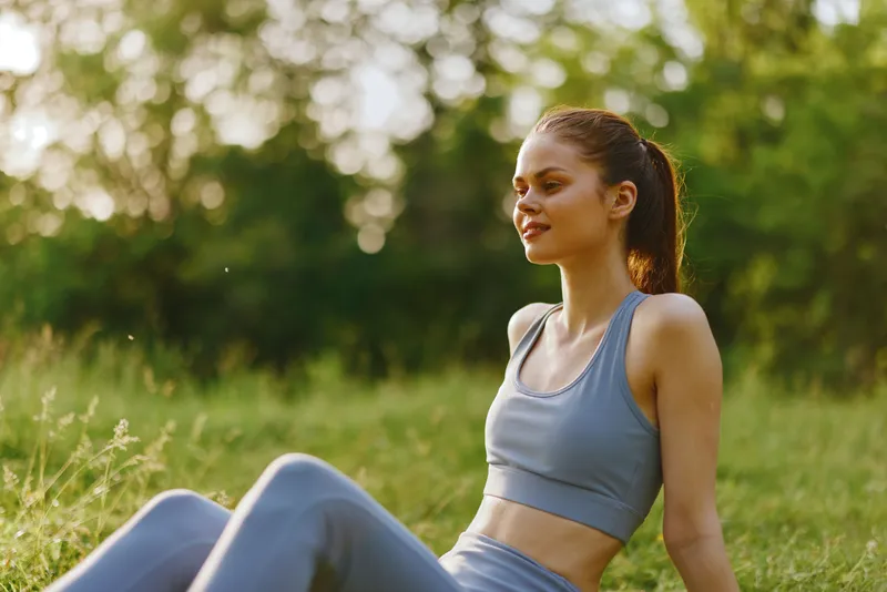 Young woman in sportswear enjoying a sunny day outdoors, conveying relaxation and wellness in a vibrant green setting