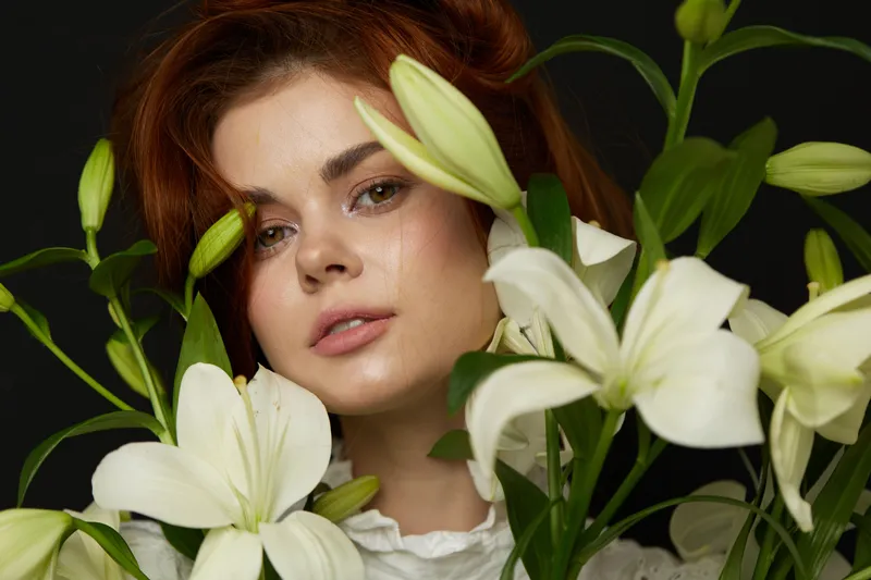 A young woman with red hair surrounded by white lilies, showcasing elegance and natural beauty, perfect for concepts like beauty, nature, and springtime