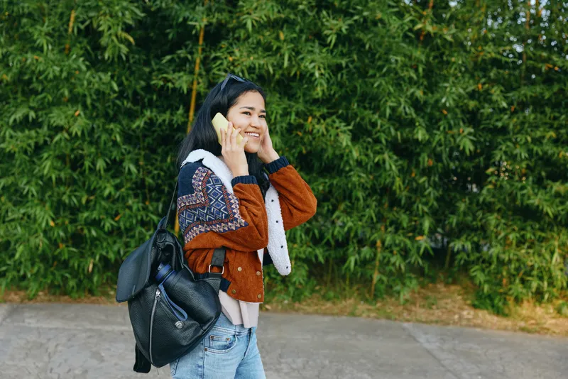 woman phone outdoor backpack street casual lifestyle smiling urban fashion travel candid accessory youth sunshine day journey movement streetwear leisure mobility scenery green trees pavement bag