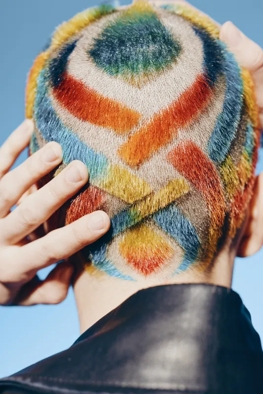 Woman with colorful geometric hair design shaved head, creative style, vibrant pattern, close-up, artistic expression, bright daylight outdoors.