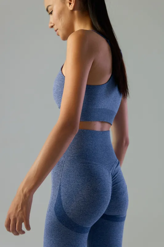 Fit woman sport fitness wearing blue seamless workout outfit, showing toned figure and healthy lifestyle, standing against plain neutral background.