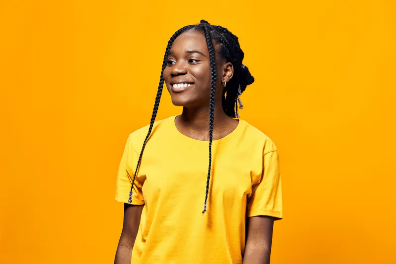 Smiling young Black woman in a yellow t shirt against a vibrant yellow background, reflecting joy, positivity, and style, perfect for lifestyle and wellness themes