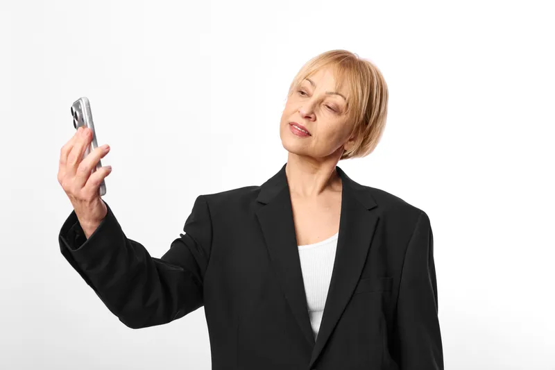 Business woman in black suit holding a smartphone on white background, turning slightly to the side, calm confident expression, studio portrait, communication