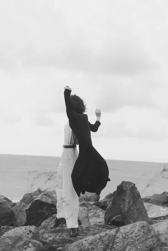 Dance, couple, silhouette on rocky shore by the sea, wind in garments and motion, black and white mood, a romantic moment of celebration on the coast and dramatic horizon
