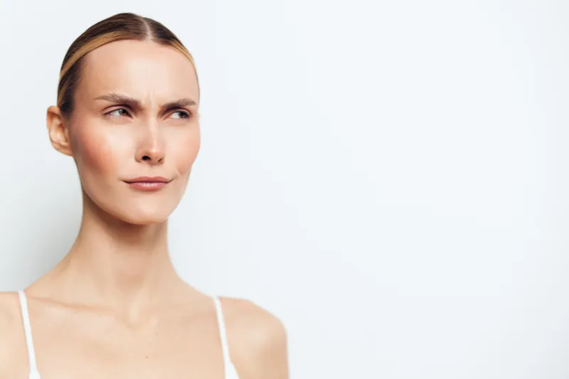 Portrait of a young woman with fair skin and blonde hair looking sideways with a skeptical expression on a white background, concept of doubt, uncertainty, and contemplation.