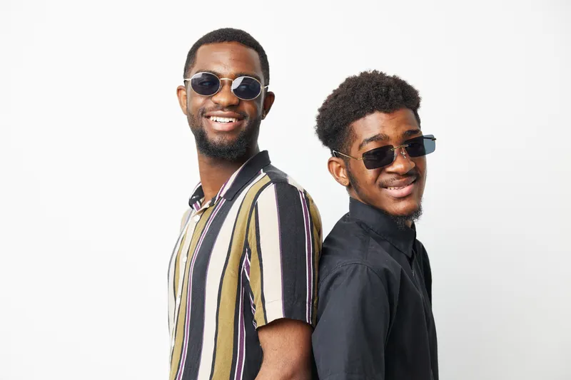 Two African American men smiling confidently, wearing stylish sunglasses and fashionable shirts. This vibrant image exudes a sense of friendship and fun.