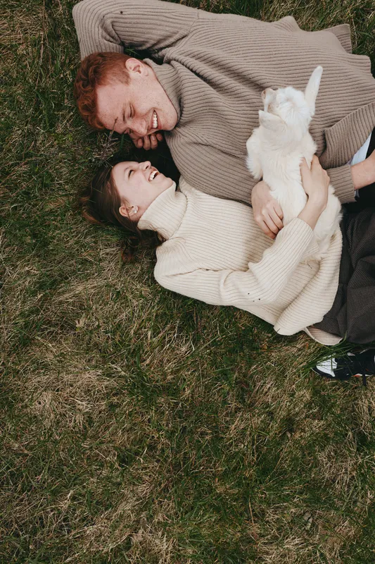 Lifestyle couple relaxing on grass with a goat kid, enjoying outdoor moments and gentle affection in a natural setting, conveying warmth, togetherness, and carefree wellness and inner peace.