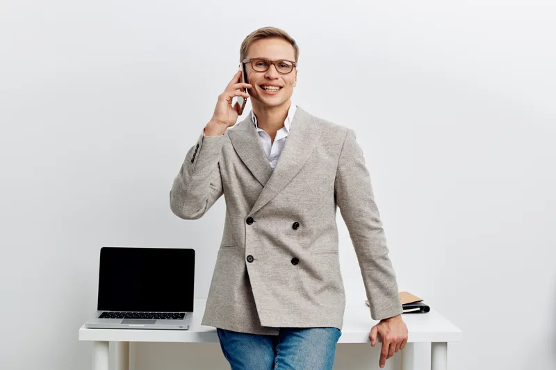 smiling man talking phone business casual wear glasses laptop desk digital nomad work remote freelance concept communication technology inside room