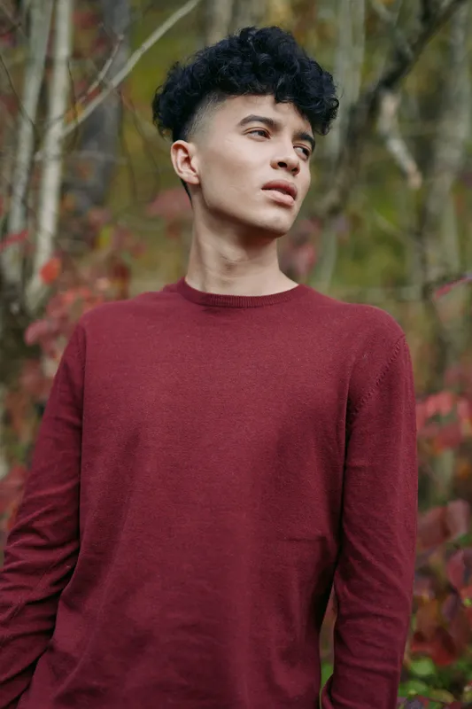 A candid portrait of a young man in a maroon sweater, photographed with natural light to convey authenticity and credibility through honest gaze and simple detail.