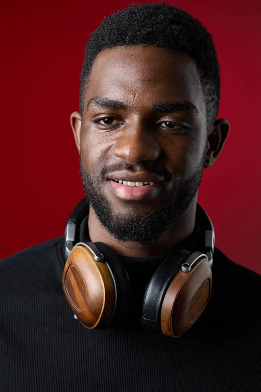 Young African man smiling with wooden headphones on his neck, vibrant red background, portrait capturing joy and modern lifestyle