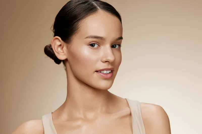 Young woman with glowing skin, wearing neutral clothing, expressing confidence against a soft beige background Perfect for beauty and skincare concepts