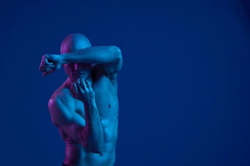 Athletic man posing in dynamic blue light, showcasing strength and flexibility, capturing a powerful moment in a visually striking composition.
