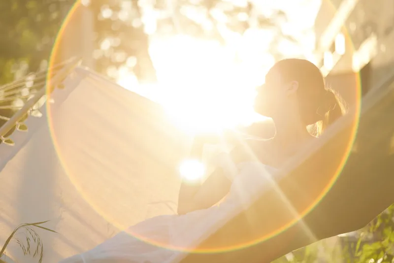 Serene woman enjoying a sunny afternoon in a hammock, radiating tranquility and joy amidst nature, perfect for themes of relaxation and self care