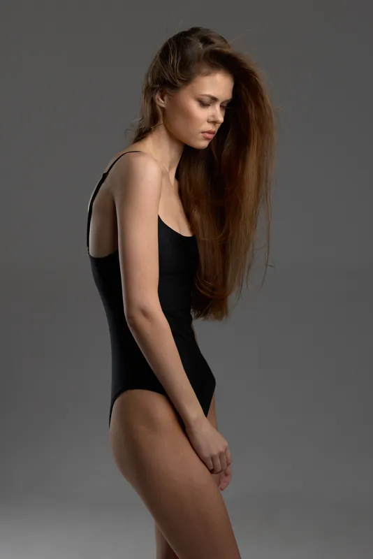 slender woman in black bodysuit with long hair posing on gray background
