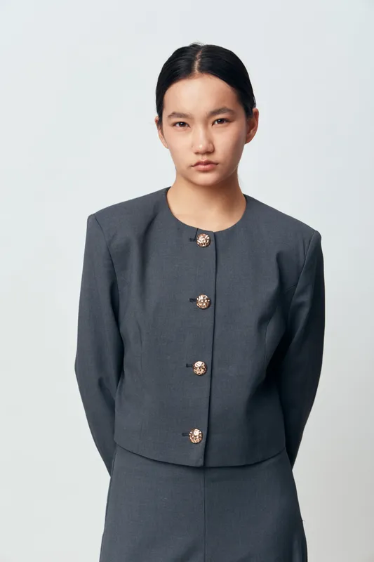 Young Asian woman in gray business suit with stylish buttons standing on white background, serious expression, professional outfit for corporate or formal occasion.