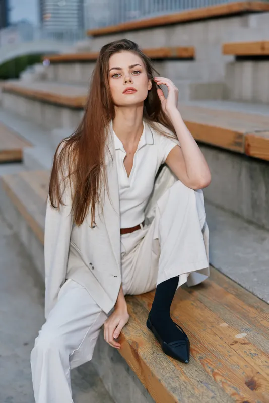 Confident businesswoman sitting on outdoor steps in a stylish outfit, showcasing elegance and determination with a modern city backdrop.