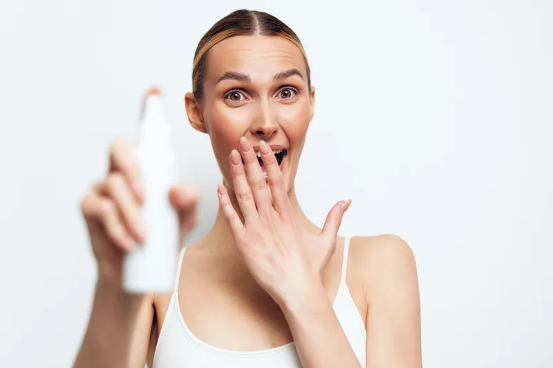 Surprised woman holding electric toothbrush in hand covering mouth with other hand on white background. Concept of dental hygiene, oral care, and healthy lifestyle.