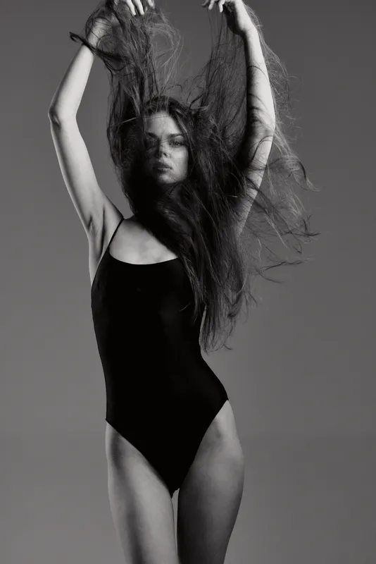 Black and white portrait of a woman with long hair wearing a black swimsuit in motion.