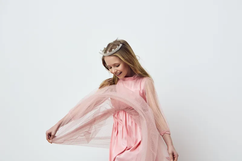 Joyful little girl in a pink dress with tulle, wearing a crown, dancing gracefully against a minimalistic white background, embodying innocence and joy