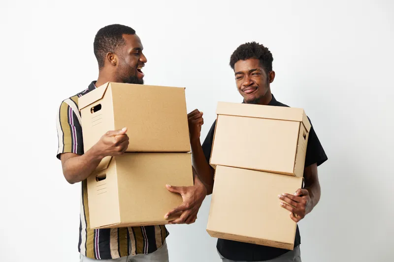 Two African American men joyfully holding cardboard boxes, conveying a sense of teamwork and collaboration in a lively environment, perfect for organizational themes.
