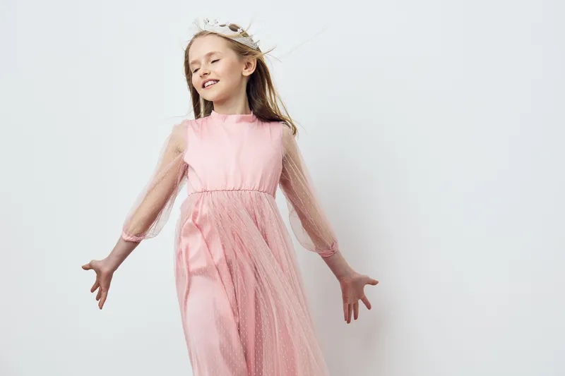 Joyful girl in a pink dress with tulle sleeves, glowing with happiness against a light background, perfect for seasonal fashion and children s portraits
